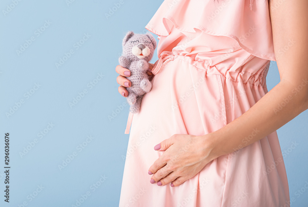 Beautiful young pregnant woman with toy on color background, closeup