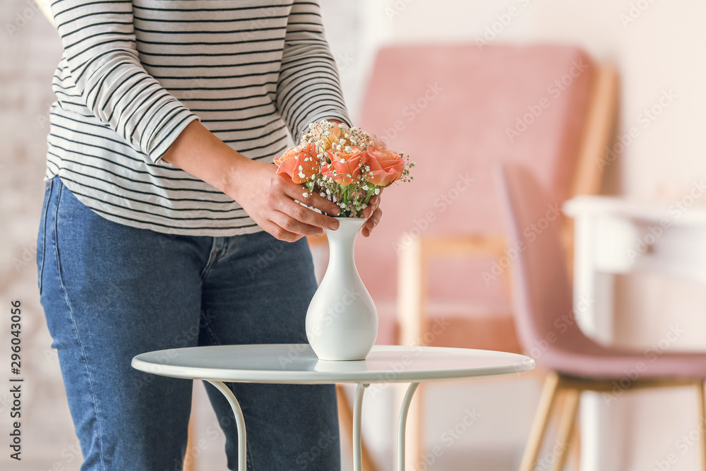 Woman with beautiful flowers in vase on table in room