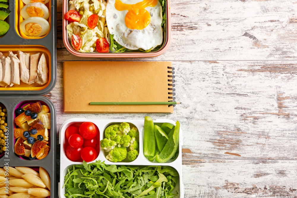 Notebook with healthy food in lunch boxes on white wooden background. Diet concept