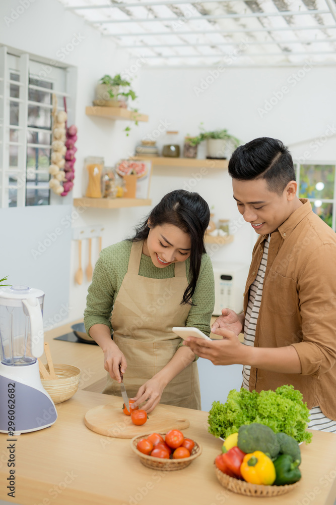 一对漂亮的年轻夫妇在家里的厨房里做饭时，正在用手机微笑