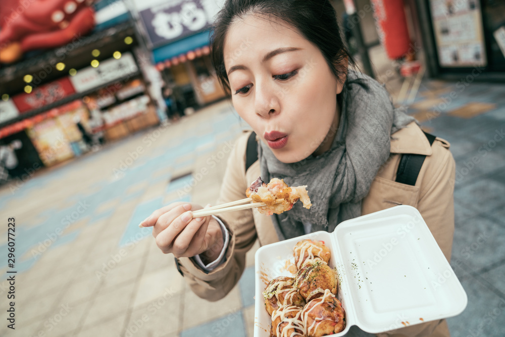 年轻的女游客在拥挤的街道上品尝日本当地的美味，背景模糊