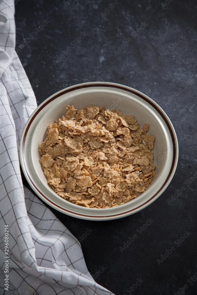 Wheat bran breakfast cereal with no milk in a bowl. Black background with homespun napkin.