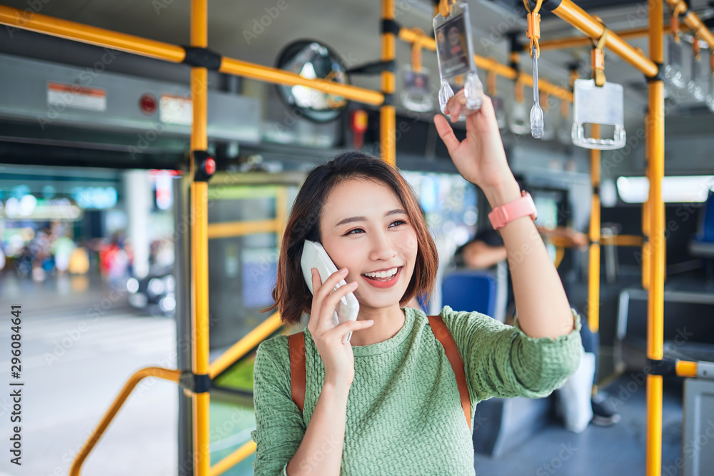 美丽的年轻女子站在城市公交车上打手机。