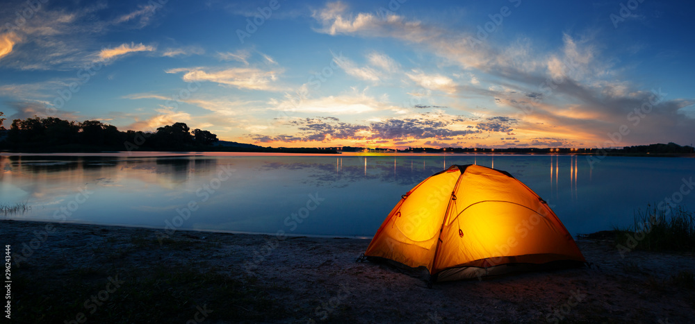 Orange tourist lit tent by the lake at sunset