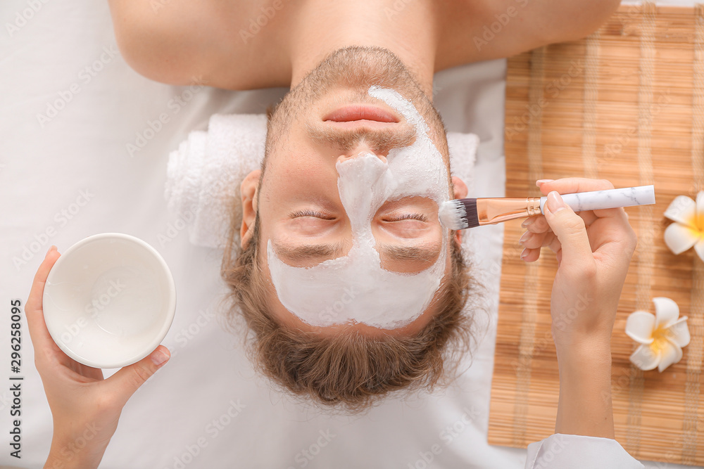 Cosmetologist applying mask onto mans face in spa salon