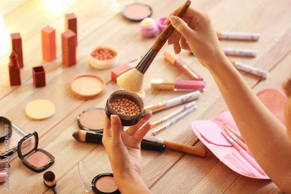 Beautiful young woman applying makeup at dressing table