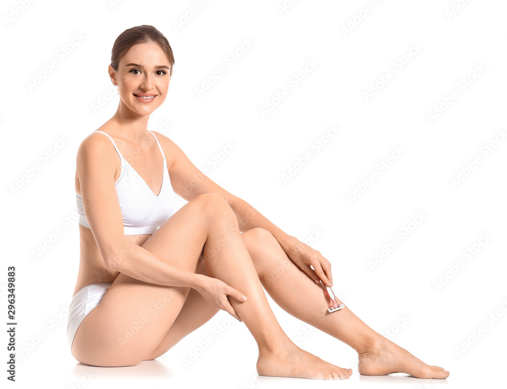 Beautiful young woman shaving legs on white background