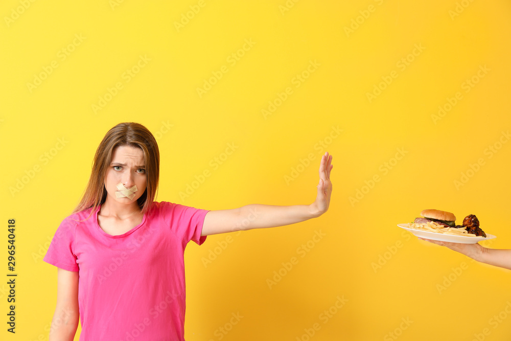 Sad woman with taped mouth refusing to eat unhealthy food on color background. Diet concept