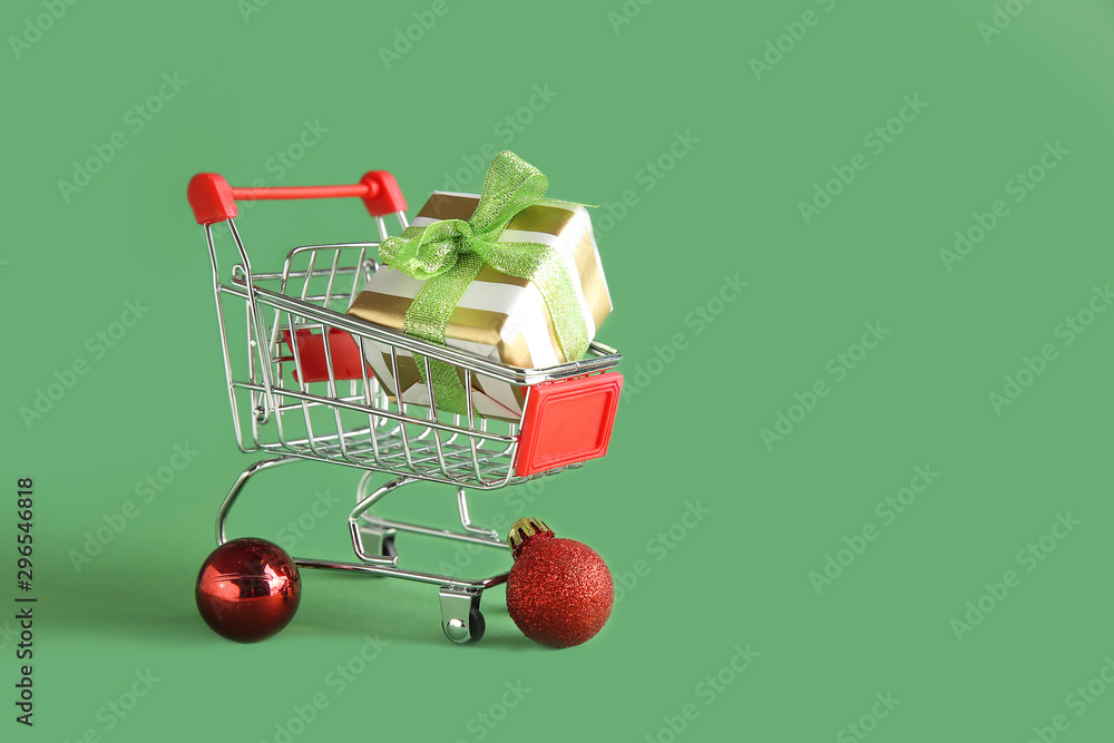 Small shopping cart with gift on color background