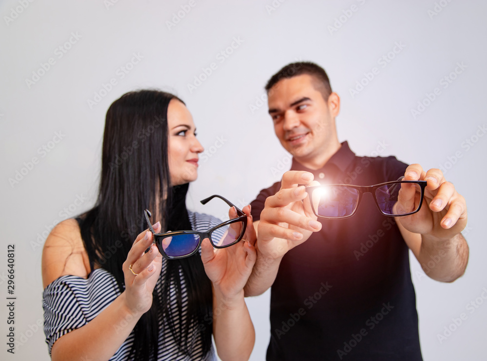 Portrait of a young couple in modern spectacles. Blurred white background. Boy and a girl hold eyegl