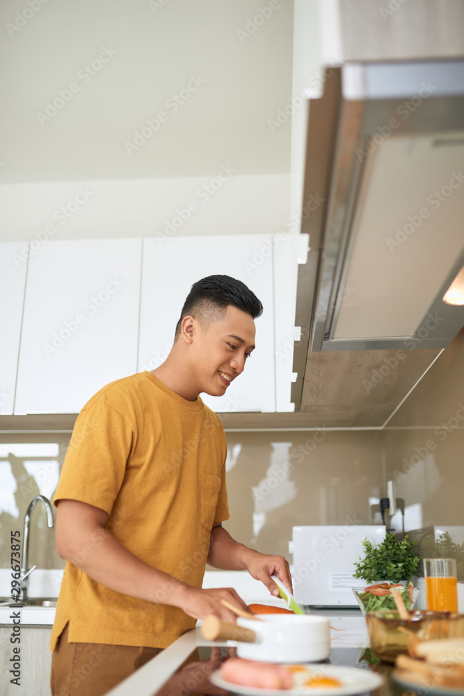 happy young man cutting vegetables in kitchen