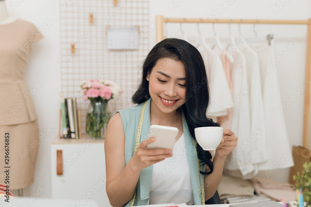 Portrait of young Asian business woman/fashion designer take a rest while drinking coffee and using 