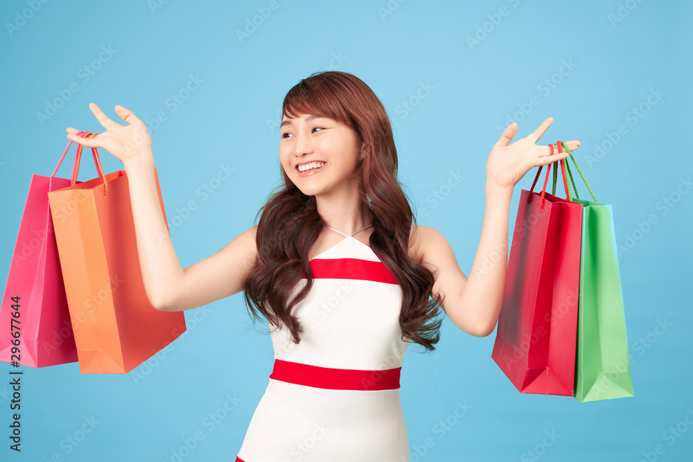 Beautiful young Asian woman with shopping bags on blue background