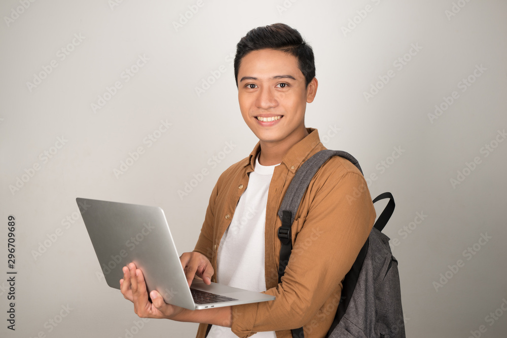 A handsome young student using laptop and carrying backpack isolated on white background