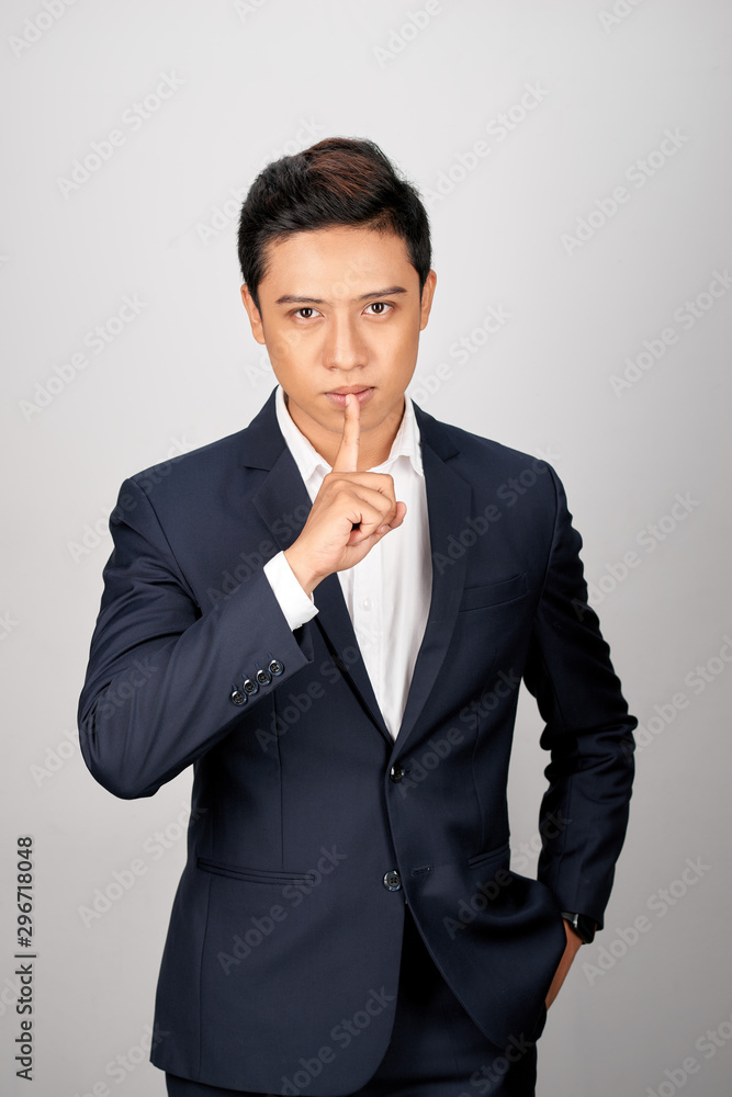 Businessman pointing finger over lips, asking for silence over white background.