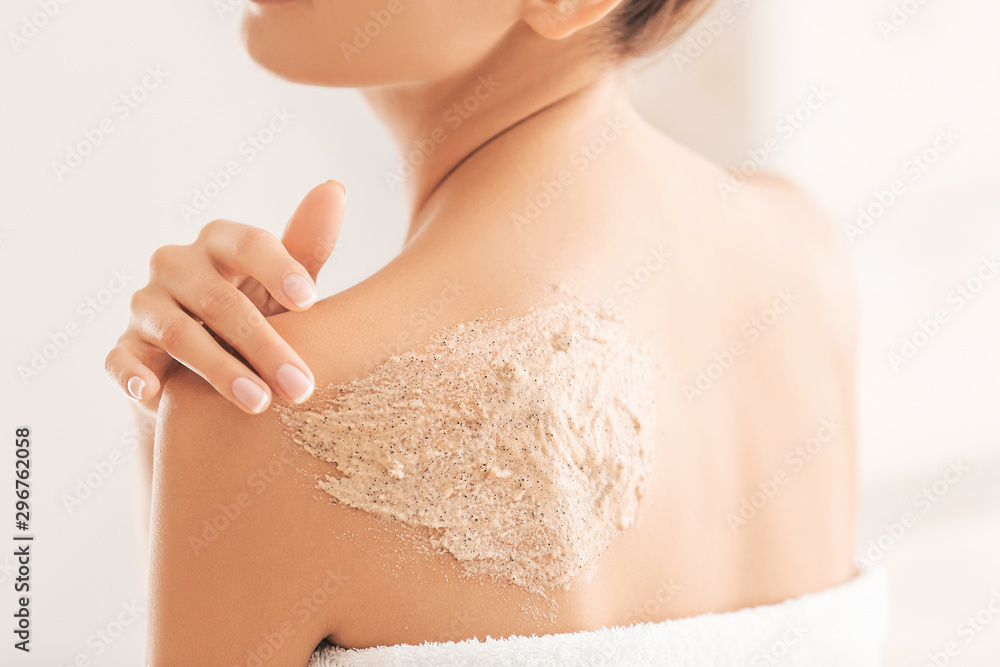 Beautiful young woman applying body scrub at home, closeup