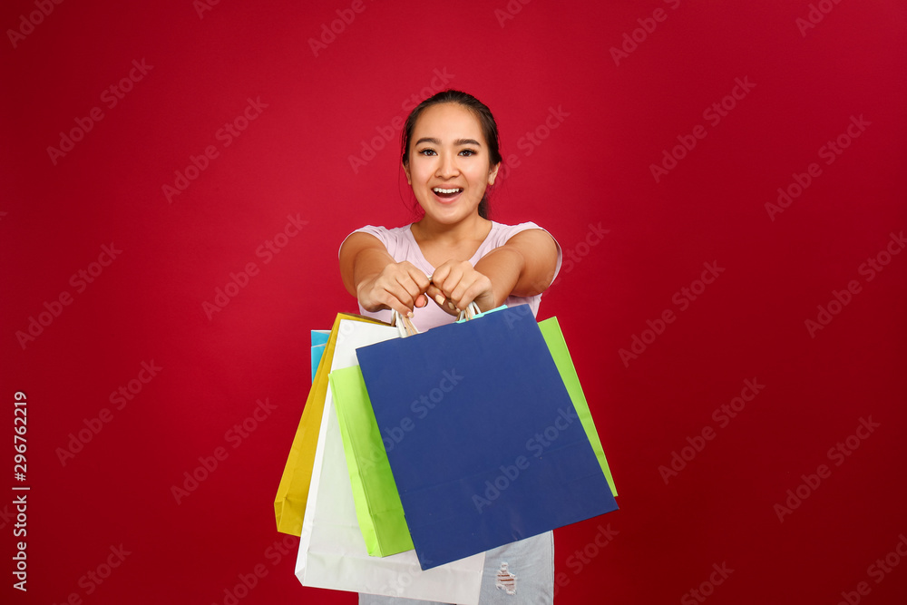 Portrait of happy Asian woman with shopping bags on color background