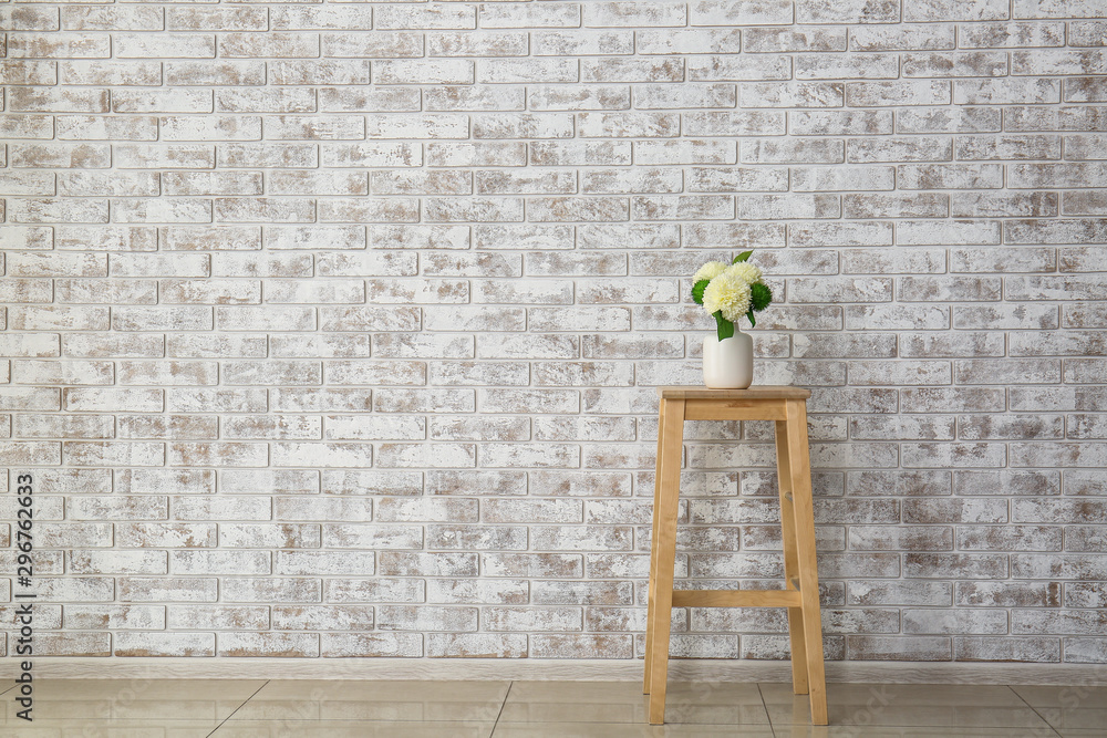 Wooden table with flowers in vase near brick wall