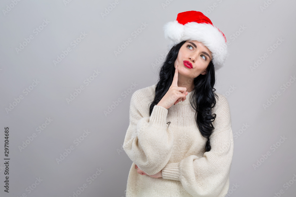 Young woman with Santa hat thoughtful pose on a gray background