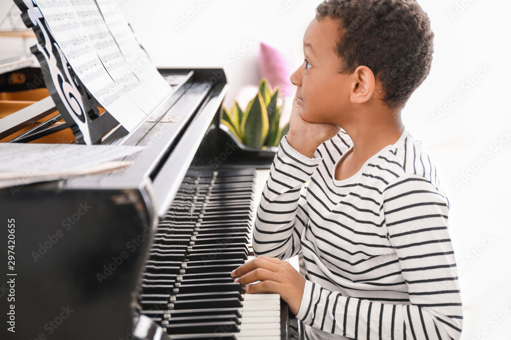 Little African-American boy playing grand piano at home