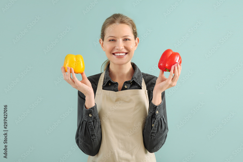 Beautiful young woman in apron and with pepper on color background