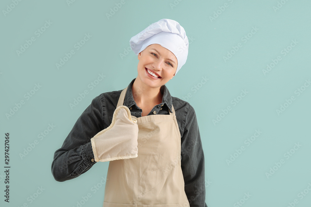 Beautiful female chef showing thumb-up on color background