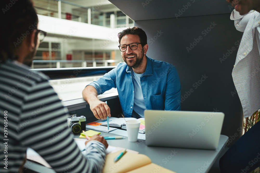 Three laughing designers working in an office meeting pod