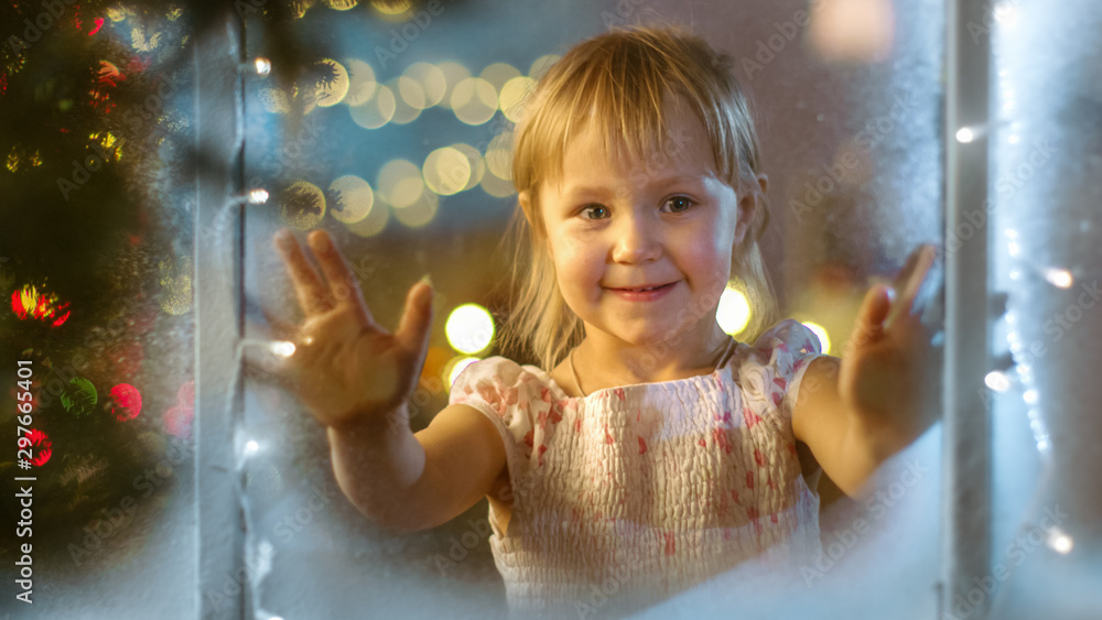 On Christmas Eve Cute Little Girl Looks Through the Window and Smiles.