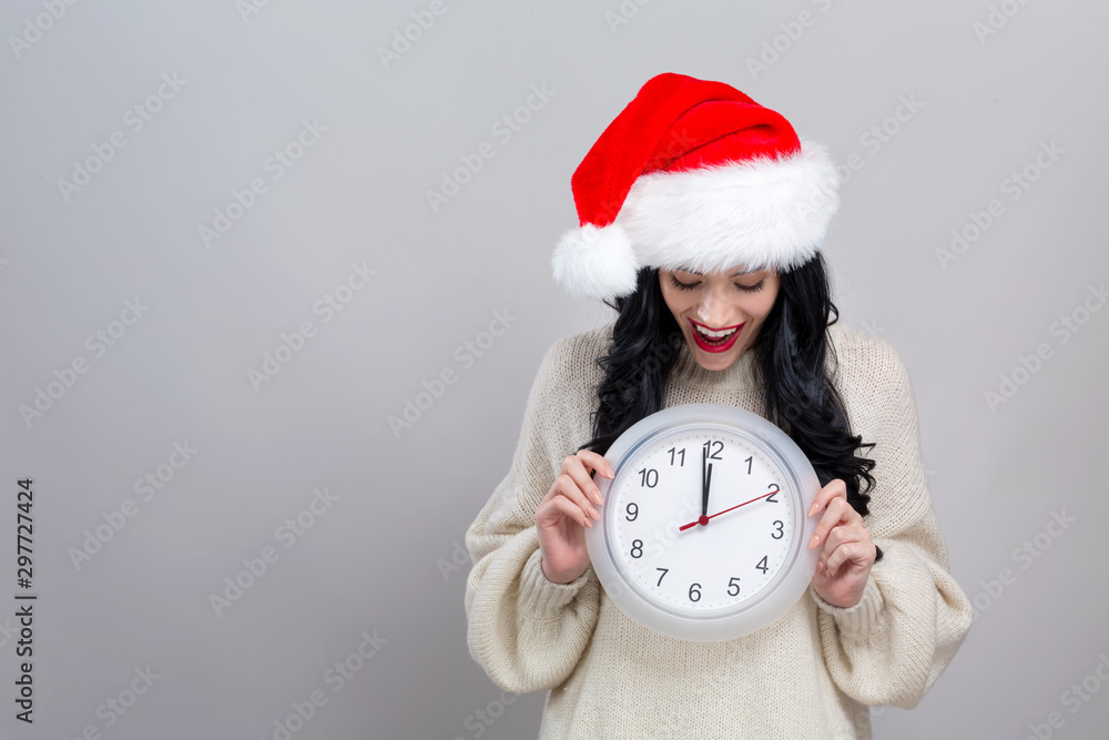 Young woman holding a clock showing nearly 12 on a gray background