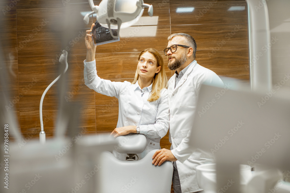 Two experienced dentists examining x-ray of a human jaw at the dental office