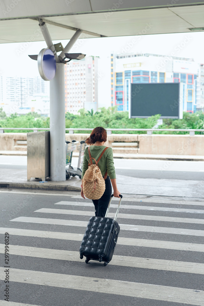 Asian female traveller crossing the road with her rolling suitcase at the airport.