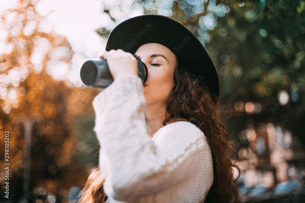 Stylish young woman walking in autumn city with thermo mug