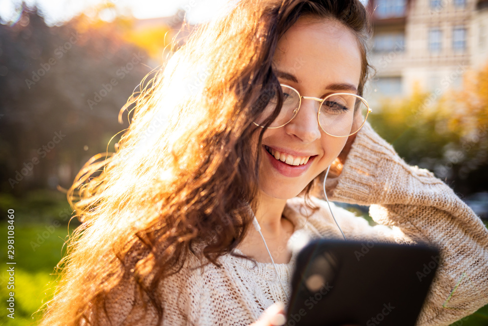 Portrait of a pretty smiling young woman using mobile phone while walking on city street