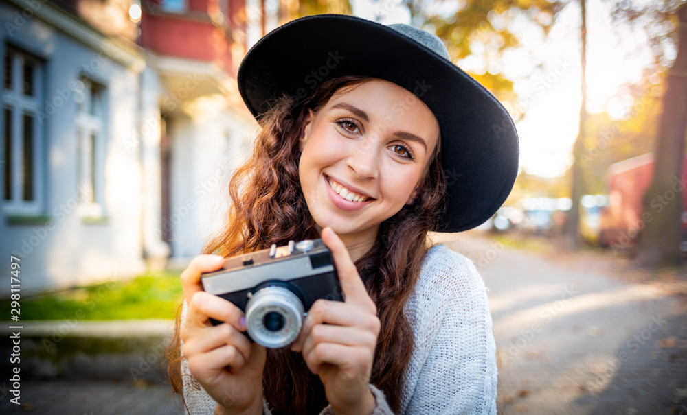 Beautiful stylish woman on city street at sunny day holding vintage retro camera