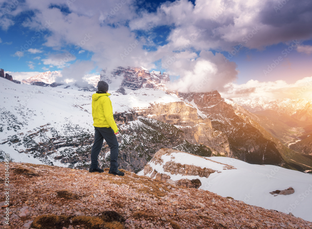 Young man in yellow jacket on the hill against snowy mountains at sunset in autumn. Landscape with s