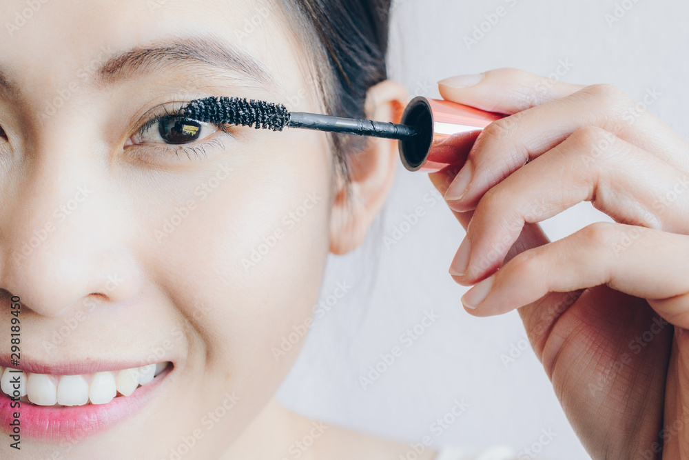 Closeup of young Asian woman applying black mascara on her eyelashes with makeup brush. Mascara is a