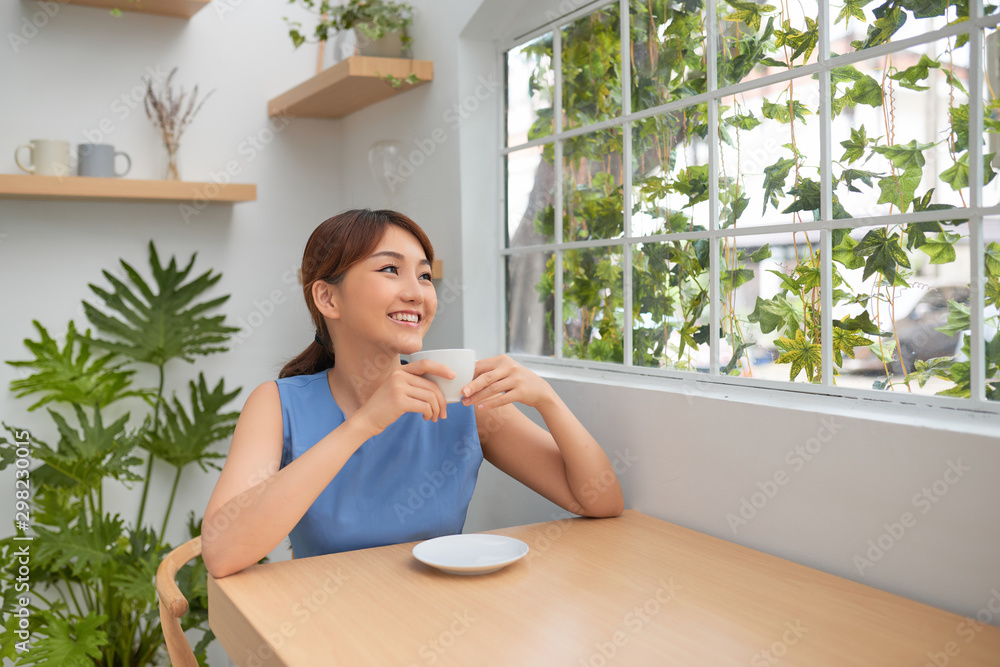 美丽的亚洲女人在绿色窗户后喝咖啡