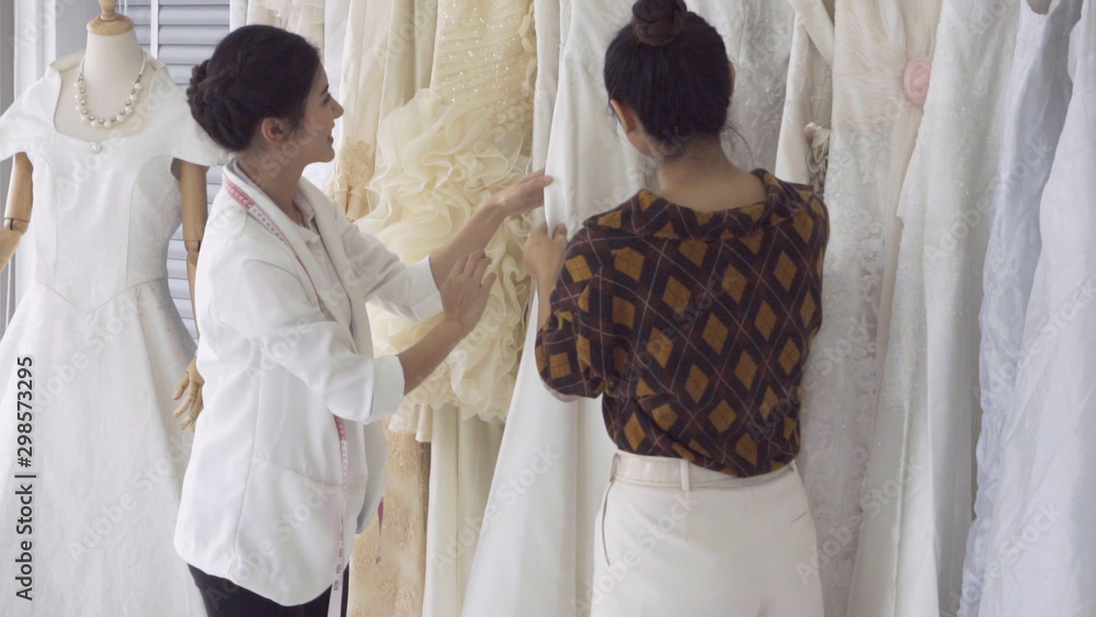 Future bride customer talking with wedding store shopkeeper to buy wedding dress and accessories for