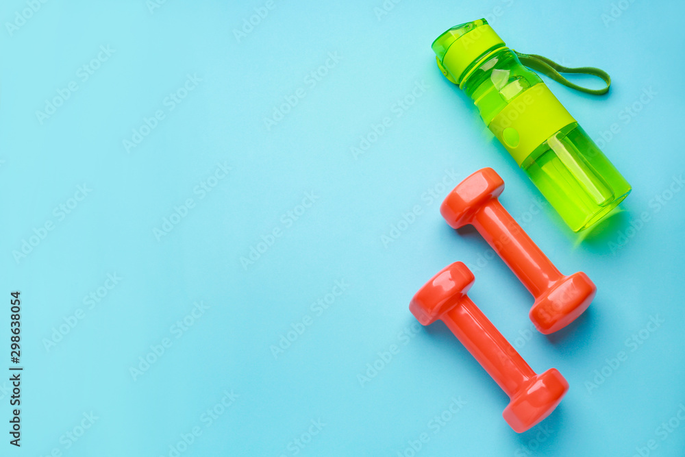 Sports water bottle and dumbbells on color background