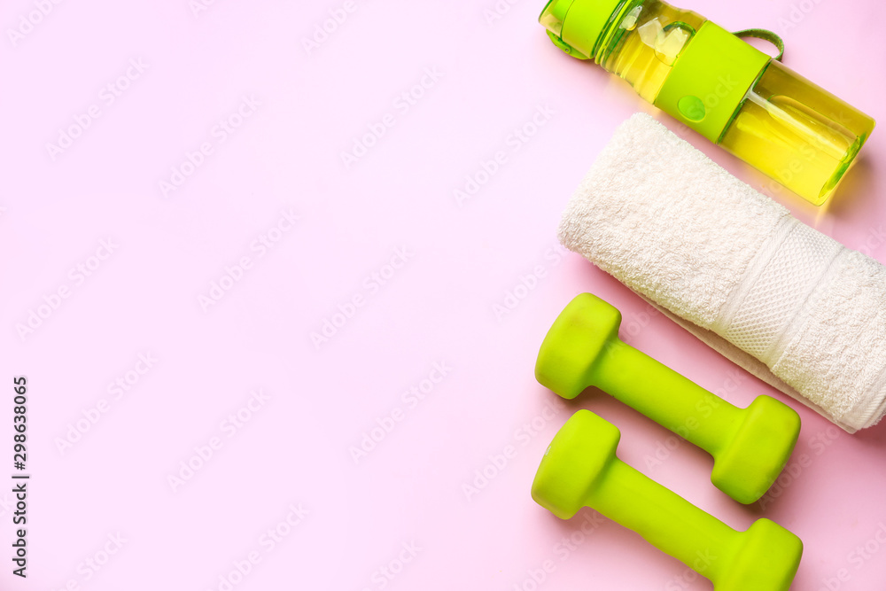 Sports water bottle, towel and dumbbells on color background