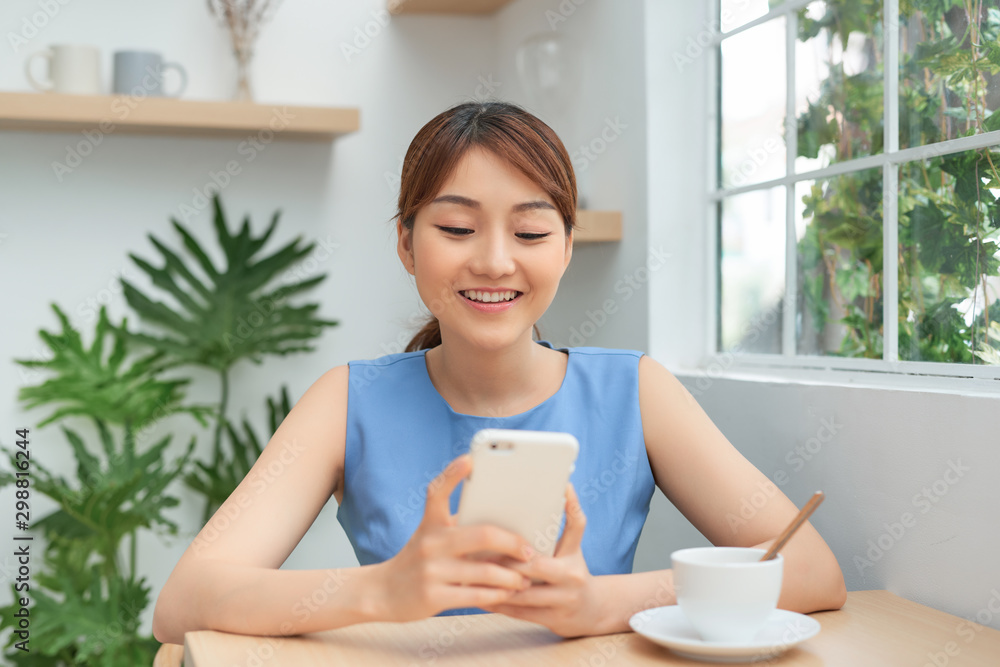 Happy young Asian woman using smartphone and drinking coffee at the table