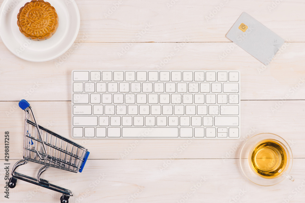 Online shopping concept. Computer keyboard, shopping cart, cake and tea with copy space.