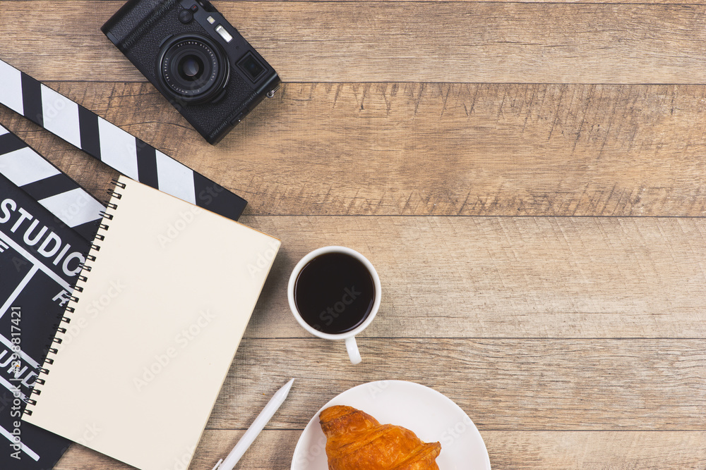 Movie clapper with paper, pen, cake and cup of coffee on wooden planks background