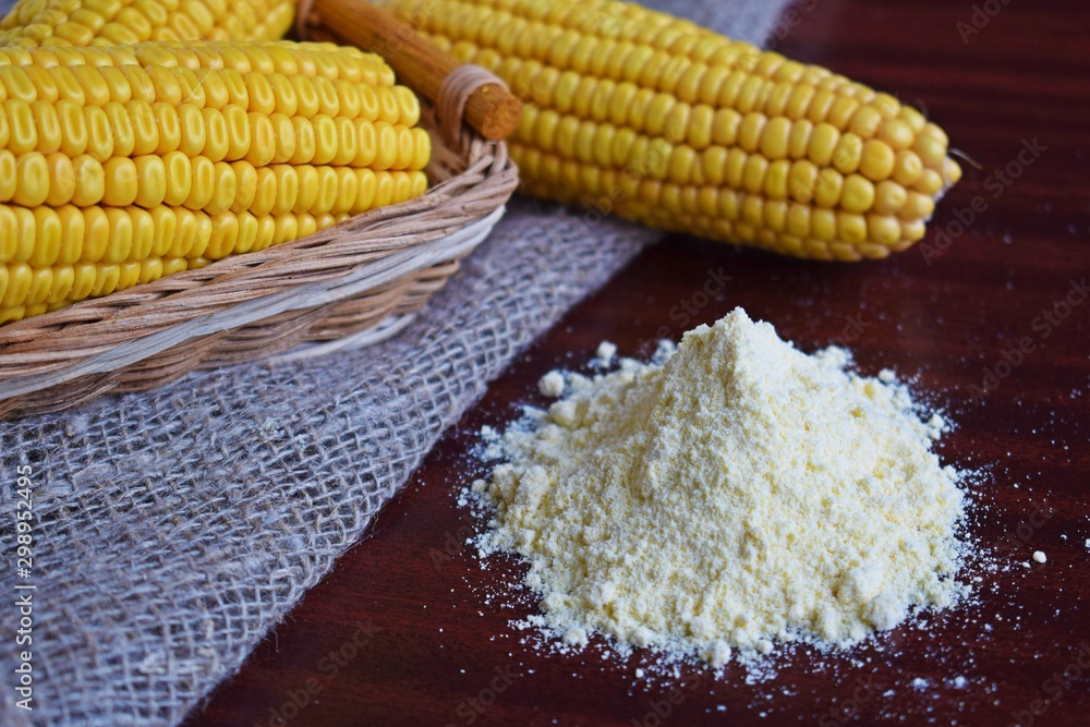 Corn flour and fresh cobs on a wooden background.