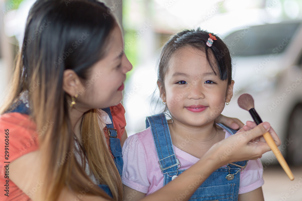 asian mother face painting her little daughter at home.