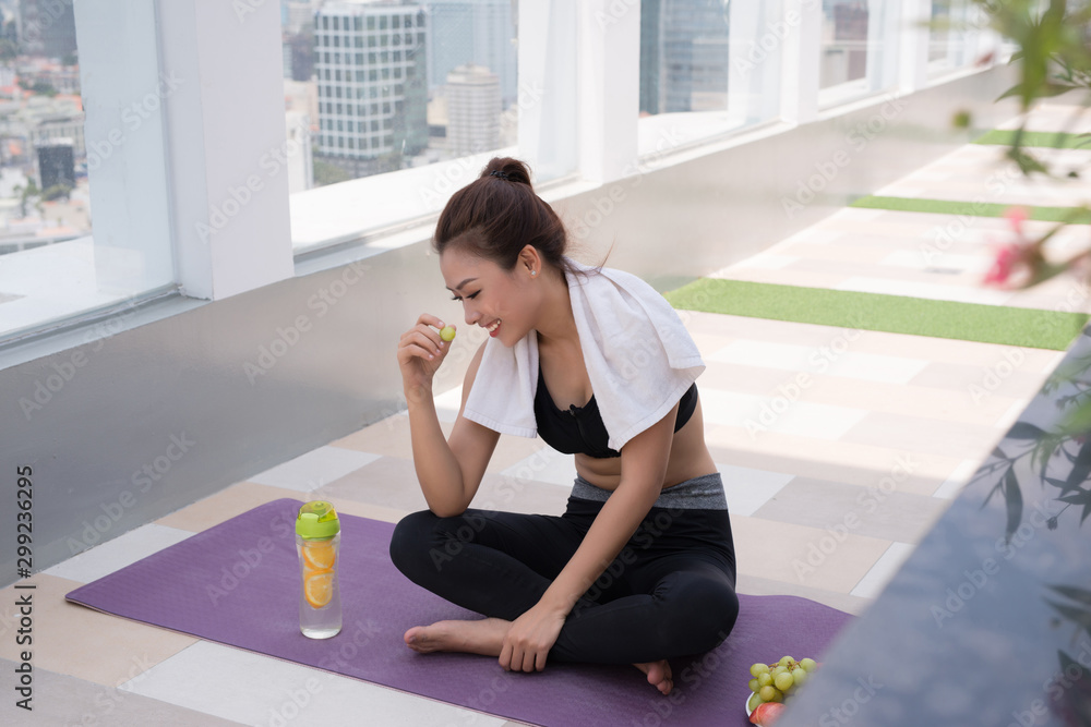 一位美丽的年轻女子坐在瑜伽垫上，在一个建筑屋顶上剧烈锻炼后休息