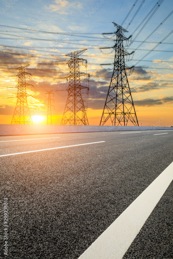 Empty asphalt road and high voltage electricity tower landscape at sunset.