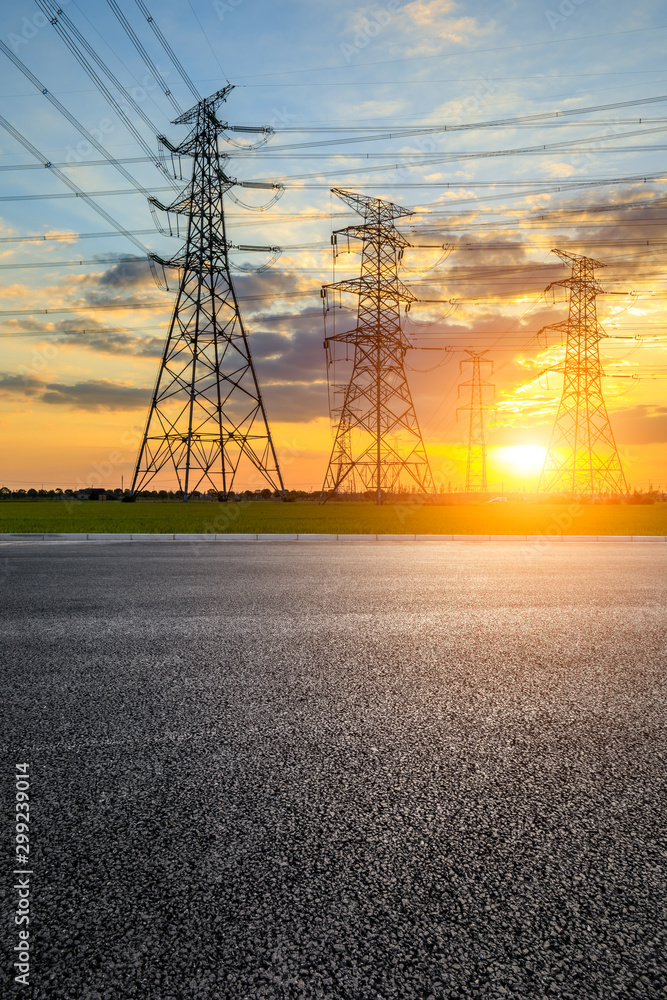 Empty asphalt road and high voltage electricity tower landscape at sunset.