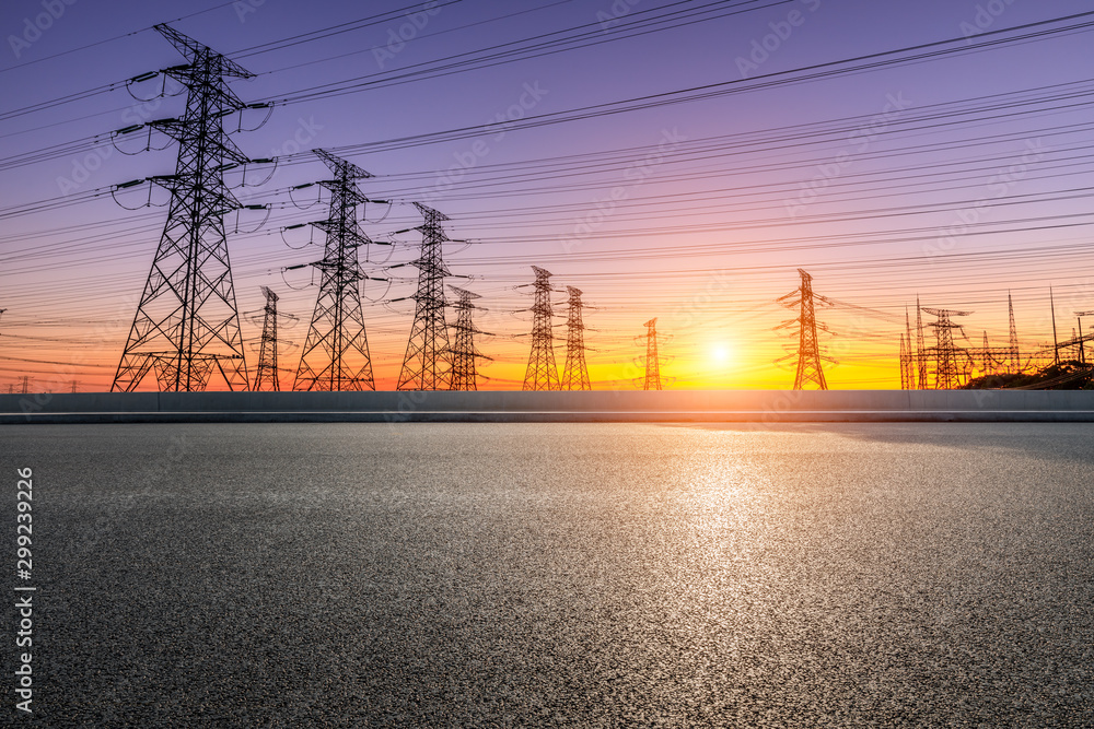 Empty asphalt road and high voltage electricity tower landscape at sunset.