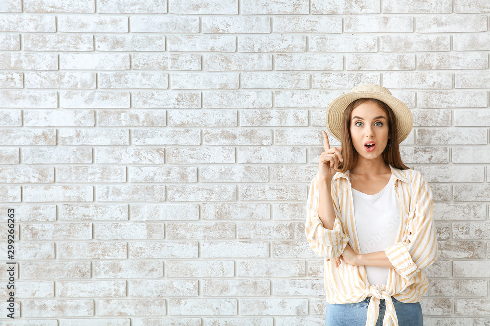 Surprised young woman with raised index finger against brick wall